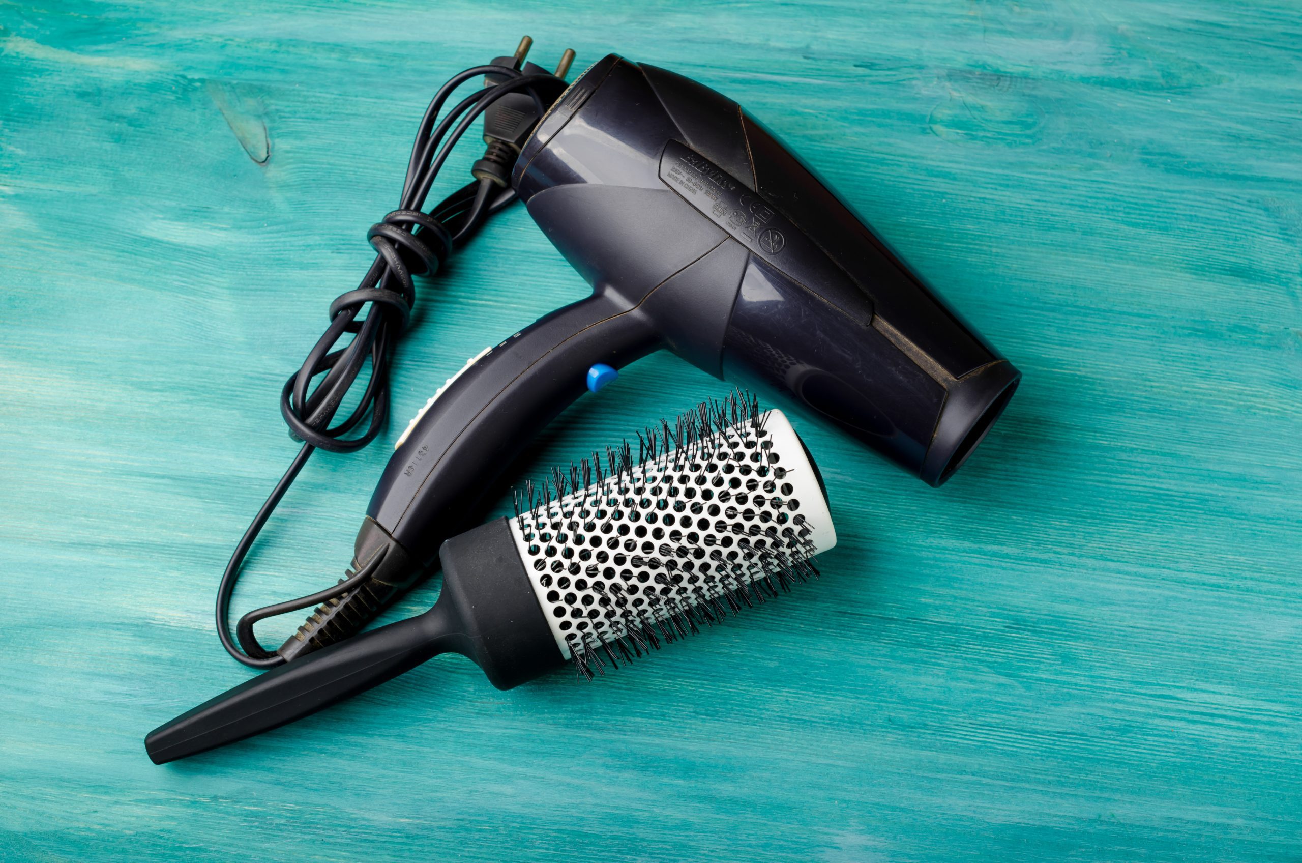 Round hairbrush and hairdryer on blue wood background