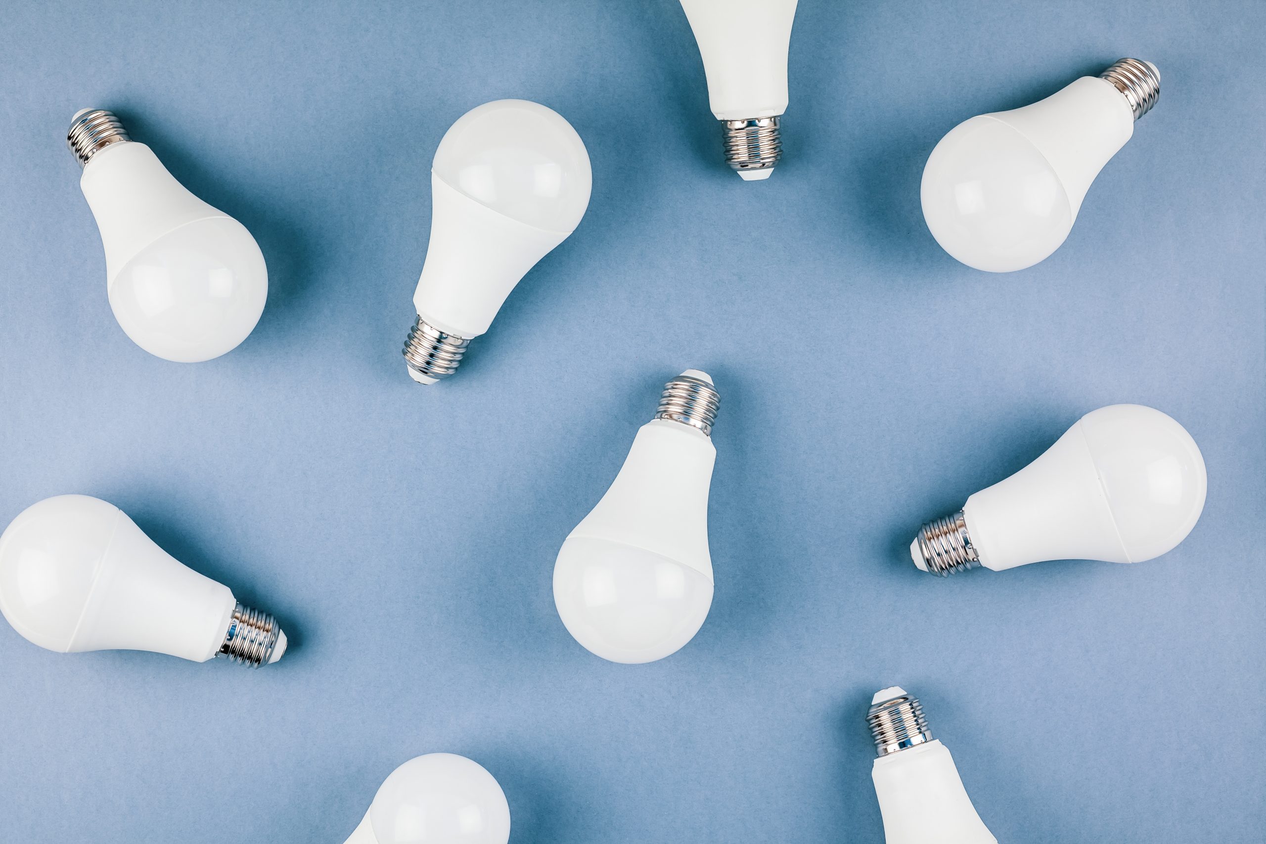 Energy-saving and eco-friendly life in conceptual frame pattern. Creative top view flat lay of LED light bulbs composition with copy space on blue background in minimal style.